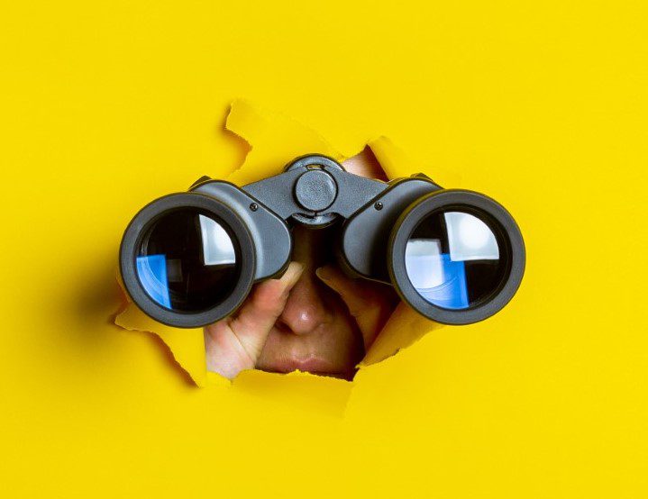 Female hand holds black binoculars on a yellow background. Journey, find and search concept. Banner