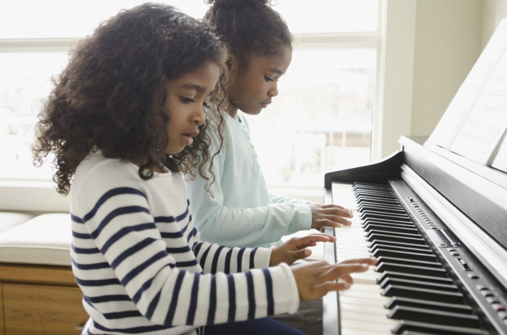 Two young girls playing a piano.